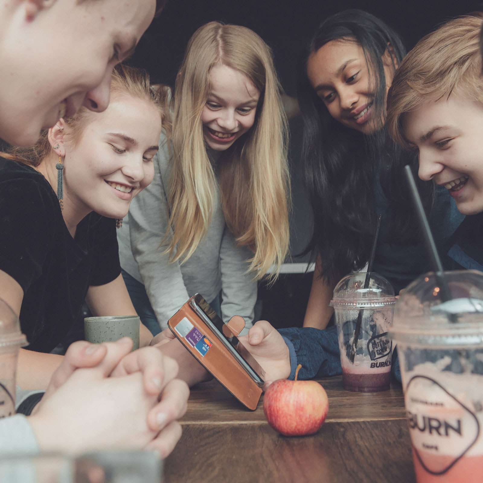 Fem teenagere ser på en mobiltelefon og griner